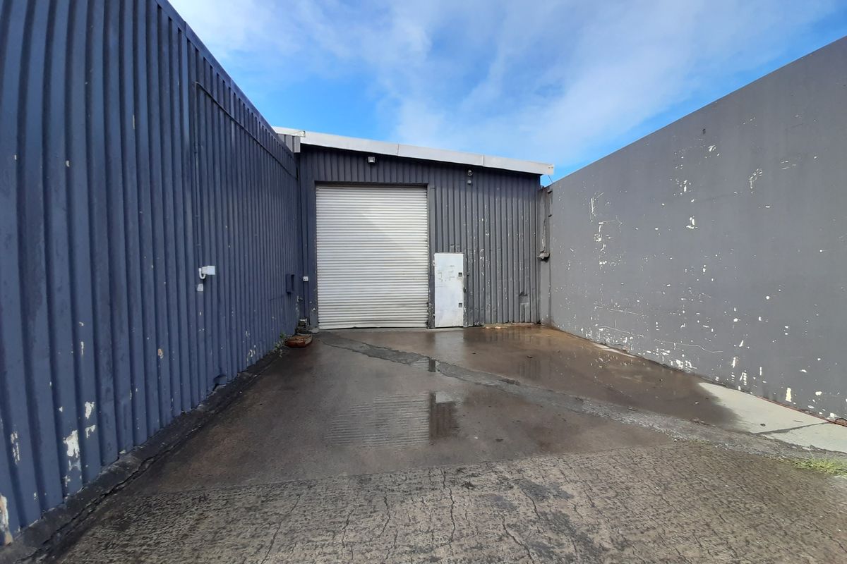 Rear industrial yard area featuring a roller shutter door, corrugated metal cladding, and a concrete hardstand surface.