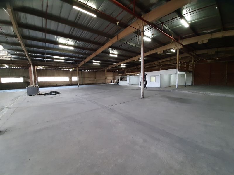 Spacious industrial warehouse featuring high ceilings with exposed steel trusses, concrete flooring, integrated fire sprinkler system, and an internal office partition.