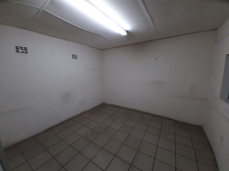 An empty utility space featuring ceramic floor tiles, a fluorescent light fixture, and wall-mounted ventilation grilles, suitable for storage or workspace use.