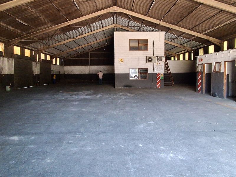 Spacious industrial warehouse featuring high-clearance steel truss roofing, concrete flooring, roller shutter access, and an integrated mezzanine office block.