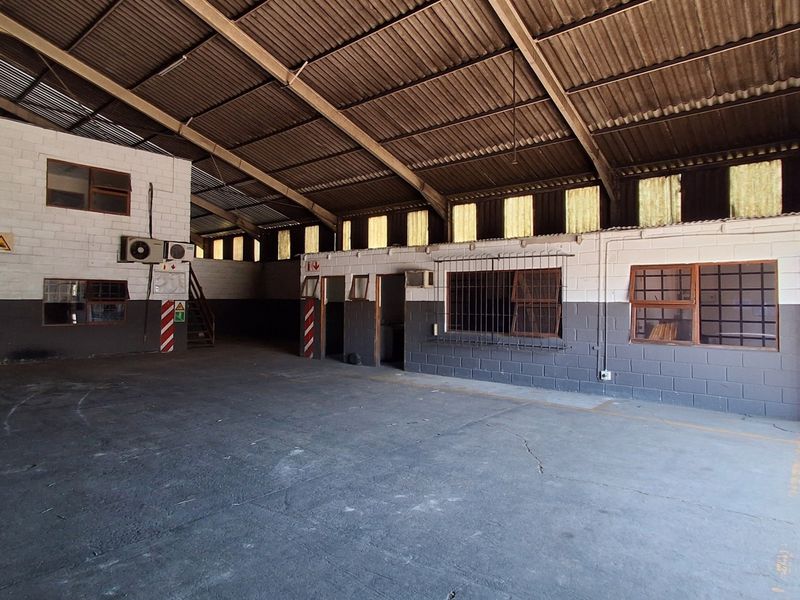 Spacious industrial warehouse featuring high ceilings with exposed steel trusses, concrete flooring, and a mezzanine level with integrated office or storage space.