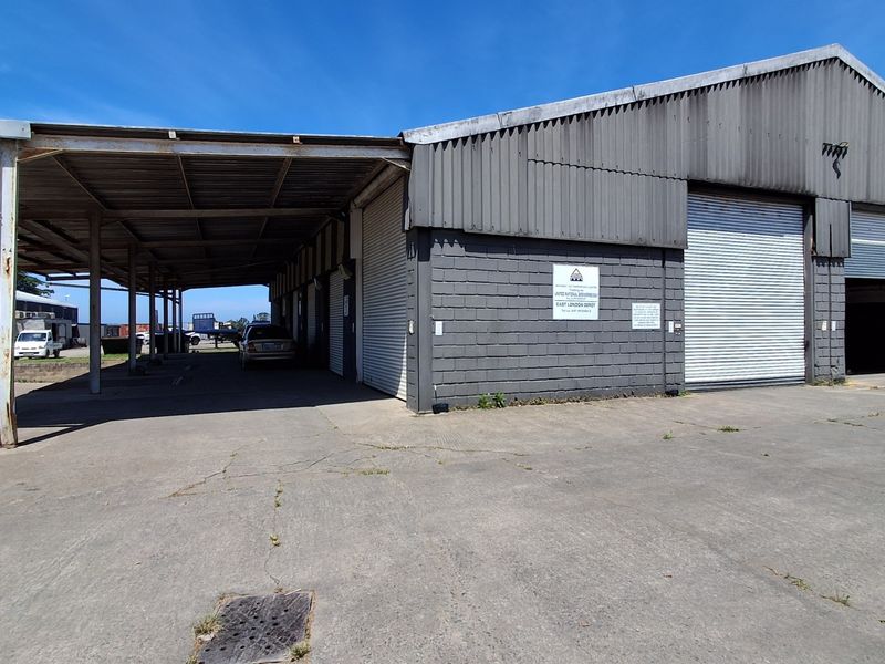 Industrial warehouse facility featuring a large covered loading area, multiple roller shutter doors, and a spacious concrete yard for vehicle access.