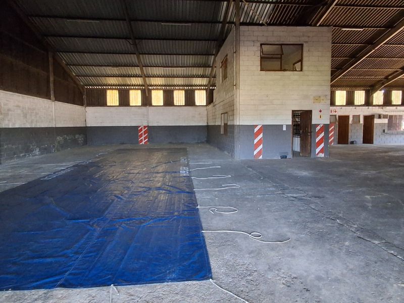 Spacious industrial warehouse area featuring high ceilings, exposed steel trusses, concrete flooring, and an integrated internal office structure.