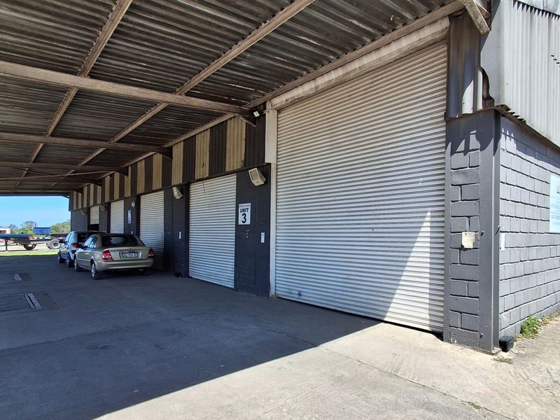 Industrial warehouse exterior featuring multiple roller shutter doors, a covered loading area with steel support columns, and durable masonry block construction.