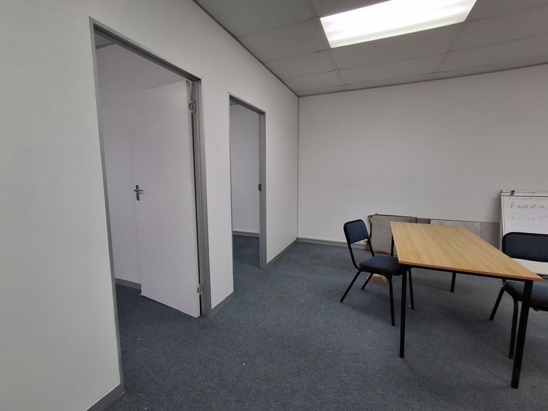 A functional office space featuring a suspended ceiling, recessed lighting, and carpeted flooring, providing a basic layout for professional use.