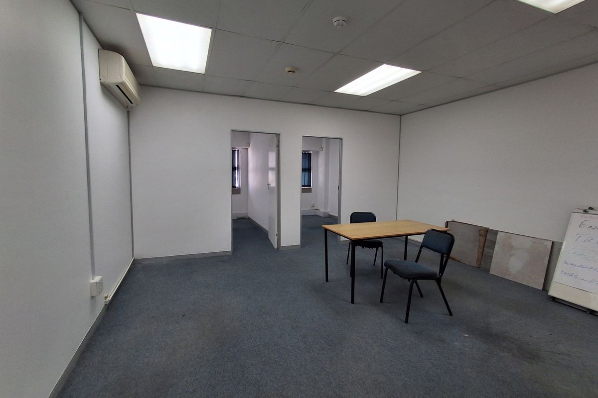 A functional office space featuring a suspended ceiling, recessed lighting, wall-mounted air conditioning, and carpeted flooring, offering a clean and professional work environment.