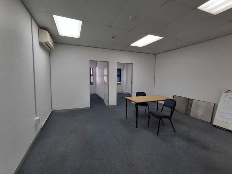 A functional office space featuring a suspended ceiling, recessed lighting, wall-mounted air conditioning, and carpeted flooring, offering a clean and professional work environment.