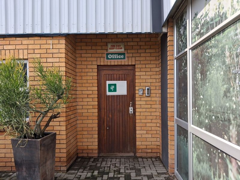 Exterior view of the office entrance featuring a brick facade, timber door, and intercom system, with a paved walkway.