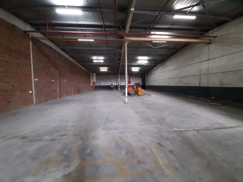 Spacious industrial warehouse unit featuring high ceilings, exposed brickwork, concrete flooring, and integrated fire safety systems, suitable for various commercial or storage applications.