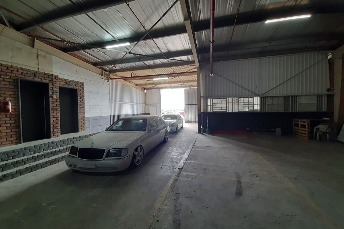 Spacious industrial garage featuring high ceilings with exposed steel structure, concrete flooring, and large sliding access doors suitable for vehicle storage or workshop use.