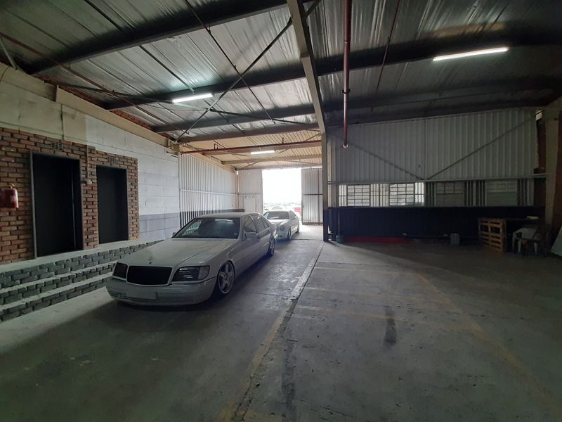 Spacious industrial garage featuring high ceilings with exposed steel structure, concrete flooring, and large sliding access doors suitable for vehicle storage or workshop use.