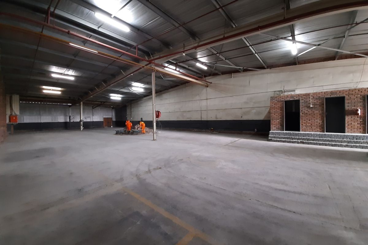 Spacious industrial warehouse area featuring high ceilings with exposed steel trusses, concrete flooring, and integrated fire sprinkler systems.