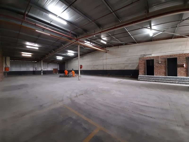 Spacious industrial warehouse area featuring high ceilings with exposed steel trusses, concrete flooring, and integrated fire sprinkler systems.