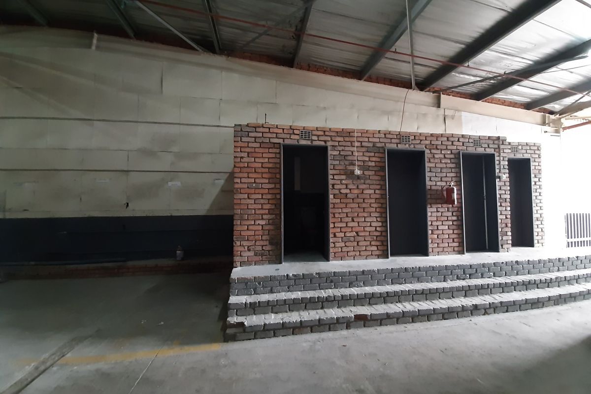 Industrial utility space featuring a brick-faced structure with multiple access points, concrete steps, and exposed roof trusses in a warehouse setting.