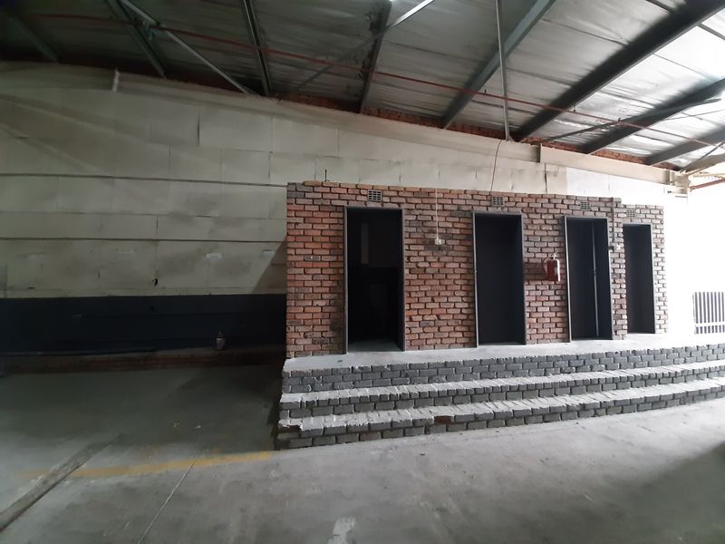 Industrial utility space featuring a brick-faced structure with multiple access points, concrete steps, and exposed roof trusses in a warehouse setting.