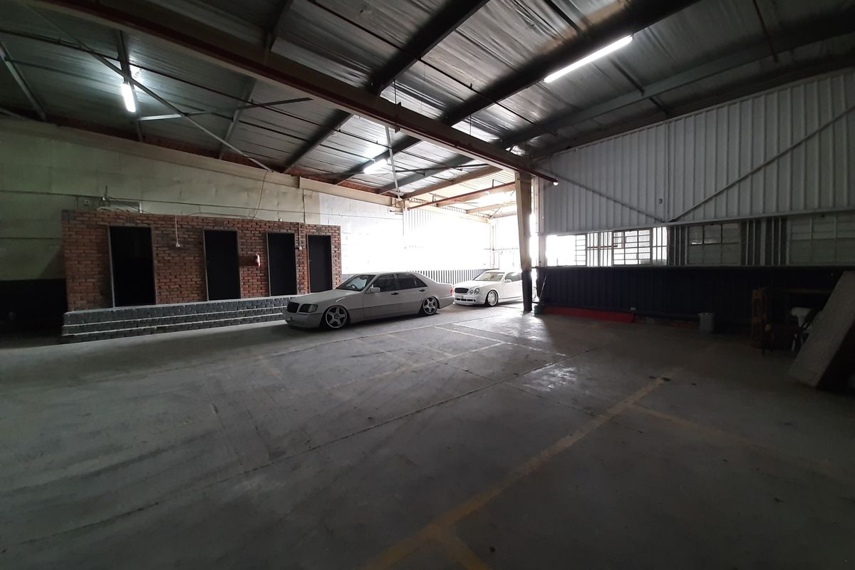 Spacious industrial garage featuring high ceilings with exposed steel trusses, concrete flooring, and a brick partition wall, suitable for storage or workshop use.