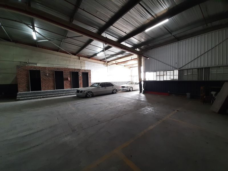 Spacious industrial garage featuring high ceilings with exposed steel trusses, concrete flooring, and a brick partition wall, suitable for storage or workshop use.