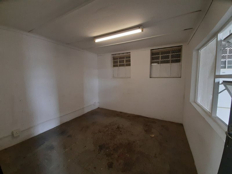 An empty utility space featuring tiled flooring, security-barred windows, and a fluorescent light fixture, requiring cosmetic refurbishment.