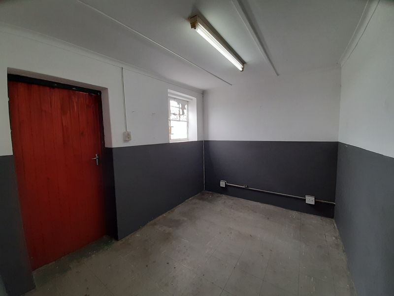 A vacant utility space featuring tiled flooring, exposed electrical conduit, and a fluorescent light fixture, suitable for storage or workshop use.