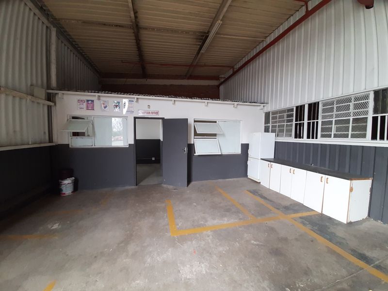 Industrial utility space featuring high-volume corrugated metal walls, exposed roof structure, built-in base cabinetry, and concrete flooring with painted bay markings.