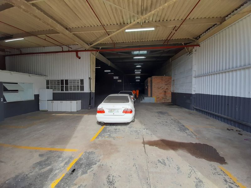 Spacious industrial garage or warehouse area featuring high corrugated metal ceilings, exposed steel trusses, and durable concrete flooring with marked parking bays.