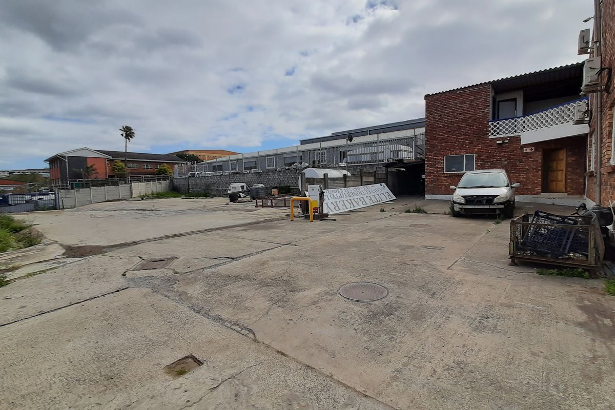 Rear exterior yard area featuring concrete paving, brick building facade, and perimeter security fencing, suitable for industrial or commercial use.