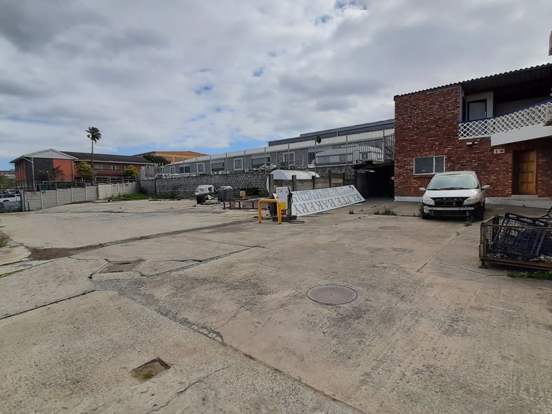Rear exterior yard area featuring concrete paving, brick building facade, and perimeter security fencing, suitable for industrial or commercial use.