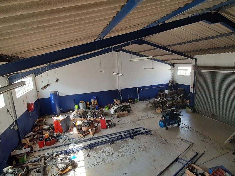 Spacious industrial utility area featuring high ceilings with exposed steel trusses, a large roller shutter door, and durable concrete flooring.