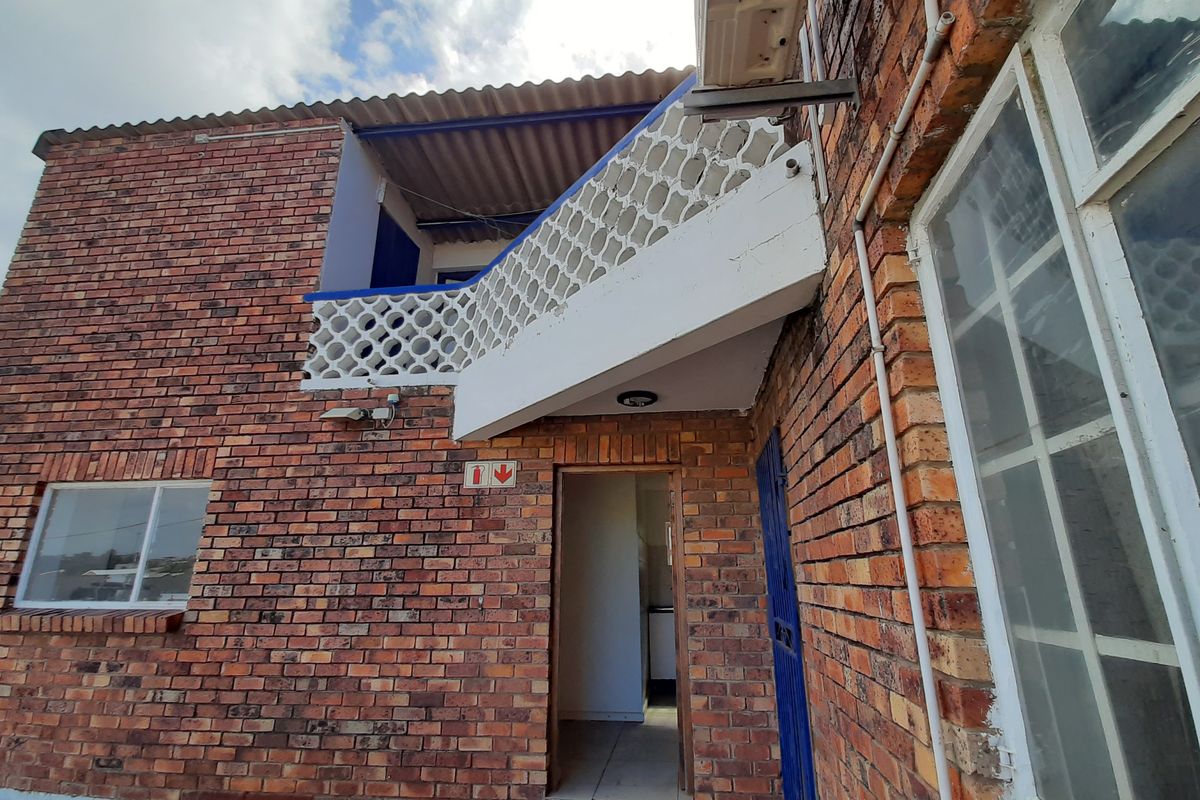 Exterior view of a brick building featuring a concrete breeze block balustrade, external air conditioning unit, and a ground-level entrance.