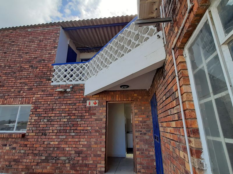 Exterior view of a brick building featuring a concrete breeze block balustrade, external air conditioning unit, and a ground-level entrance.