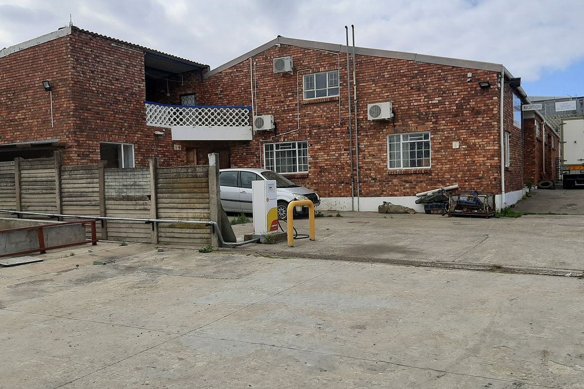 Front exterior view of a commercial face brick building featuring a concrete driveway, fuel pump, and split system air conditioning units.