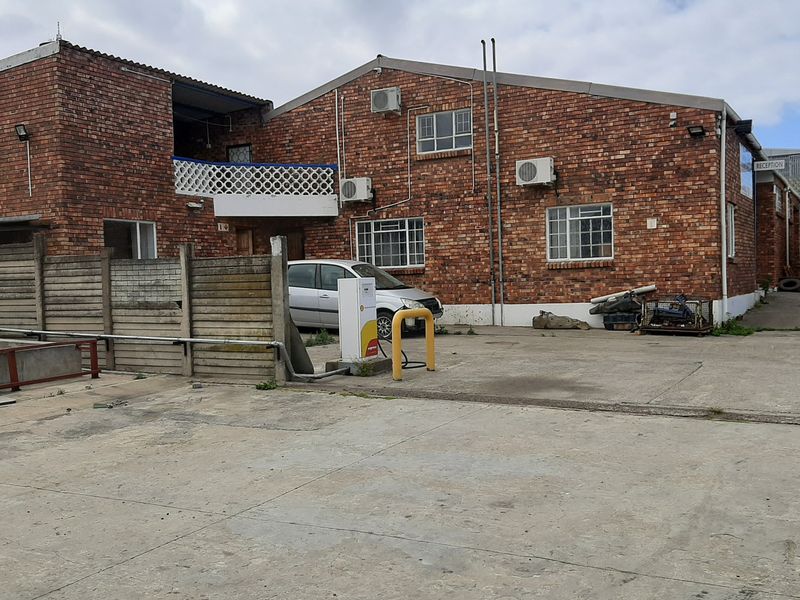 Front exterior view of a commercial face brick building featuring a concrete driveway, fuel pump, and split system air conditioning units.