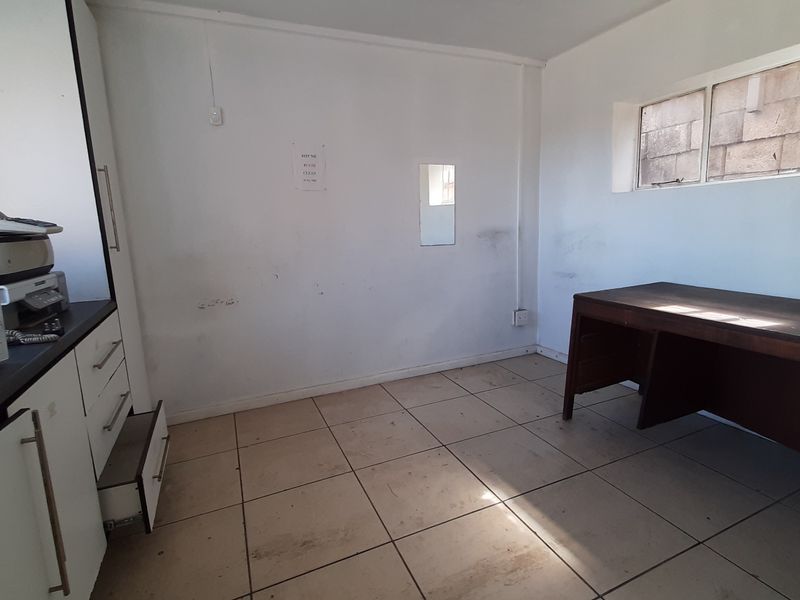 A functional office space featuring tiled flooring, built-in cabinetry, and a high-level window, currently requiring cosmetic wall and floor maintenance.