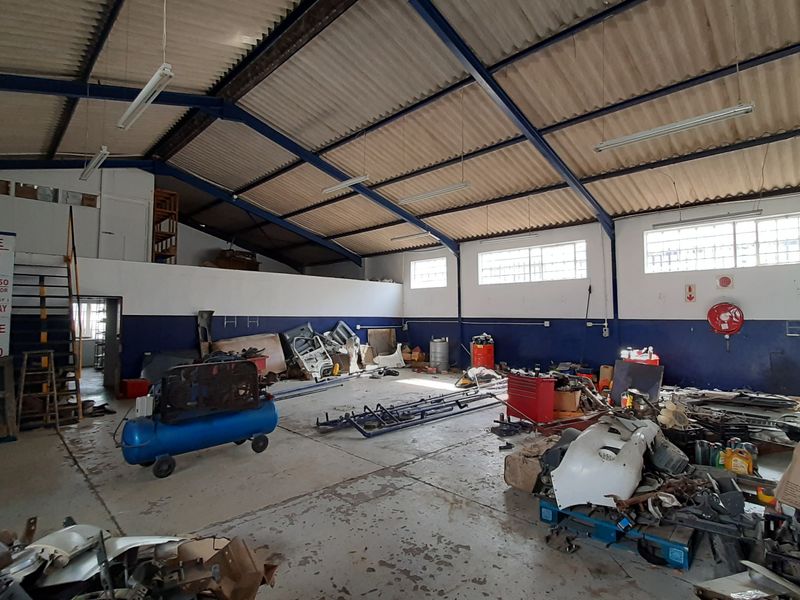 Spacious industrial garage or workshop area featuring high ceilings with exposed steel trusses, concrete flooring, and a mezzanine level for additional storage.