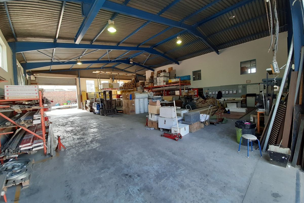Spacious industrial warehouse or utility space featuring high exposed steel trusses, concrete flooring, and a large roller shutter door for easy access.