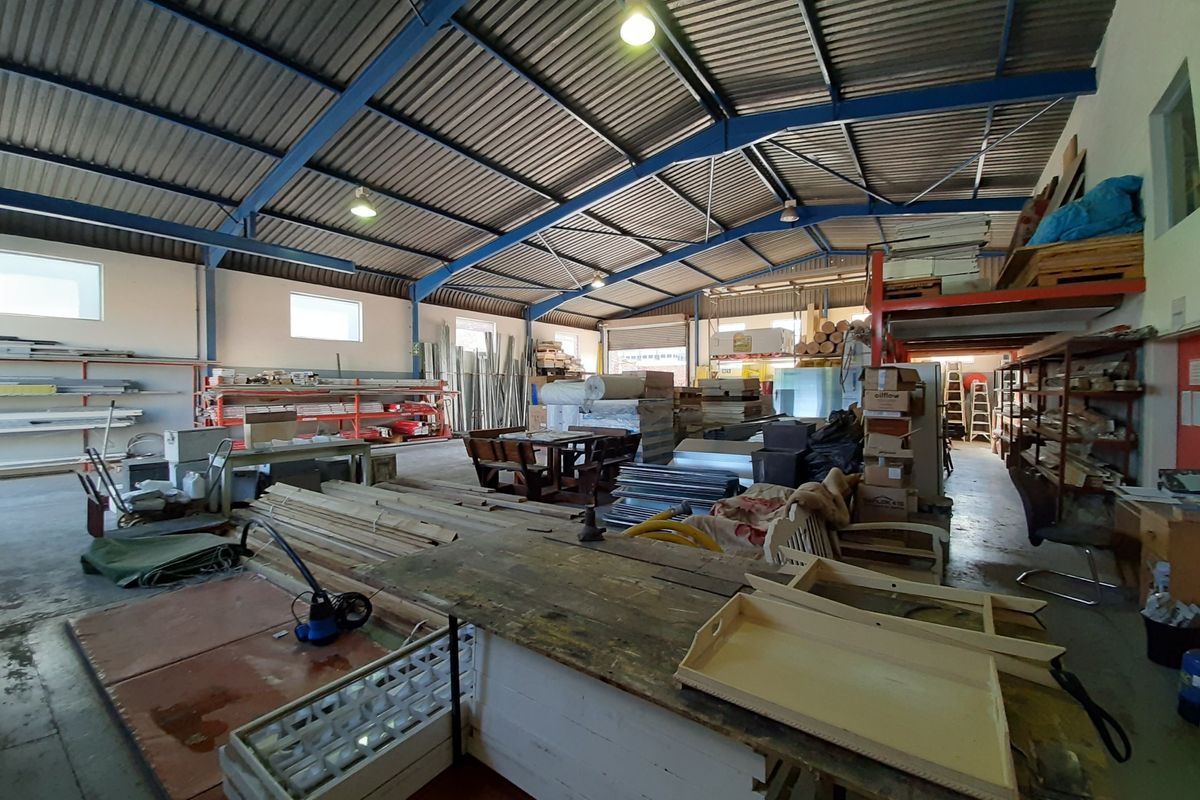 Spacious industrial utility or warehouse area featuring high ceilings with exposed steel trusses, concrete flooring, and integrated mezzanine storage racking.