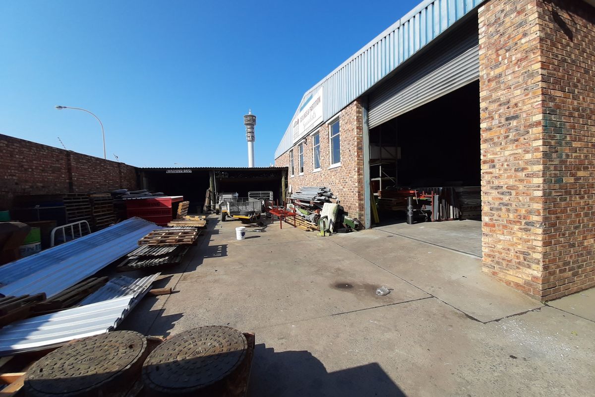 Commercial rear yard area featuring a large roller shutter door, brick facade, and concrete paving suitable for industrial storage or logistics access.