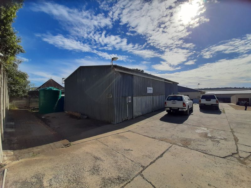 Industrial property exterior featuring corrugated metal cladding, a concrete driveway, and an external water storage tank.