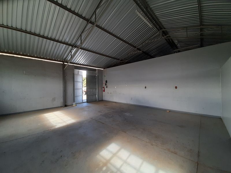 Spacious industrial utility area featuring high-clearance corrugated metal roofing, exposed steel trusses, and durable concrete flooring with direct exterior access.