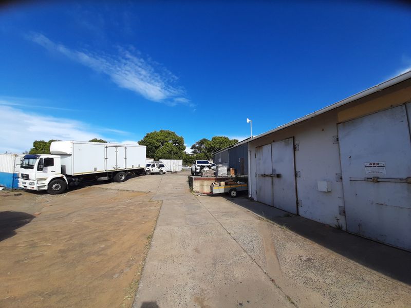 Industrial rear yard area featuring a concrete loading apron, access doors, and metal building cladding, suitable for logistics or storage operations.