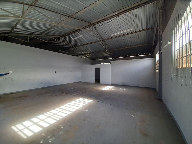 Spacious industrial utility area featuring high corrugated metal ceilings, exposed steel trusses, concrete flooring, and secure window bars.