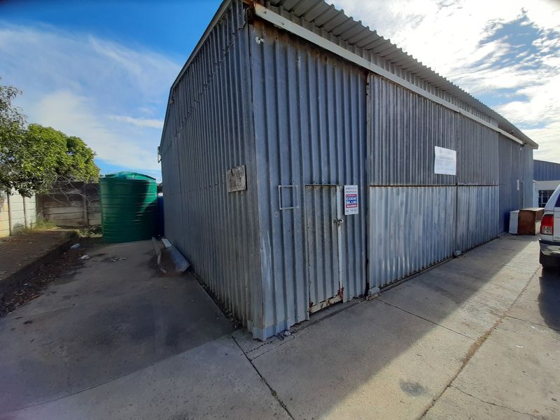 Exterior view of an industrial corrugated metal structure featuring a side access door and an adjacent water storage tank on a concrete base.
