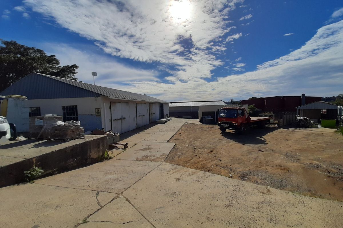 Industrial property exterior featuring a large concrete yard, warehouse structures with metal roofing, and a loading area.