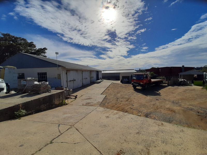 Industrial property exterior featuring a large concrete yard, warehouse structures with metal roofing, and a loading area.