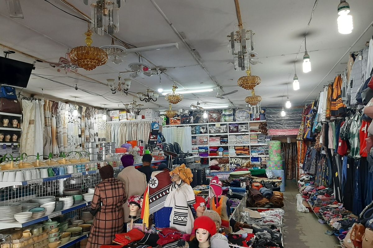 A commercial retail space featuring built-in shelving units, multiple ceiling-mounted chandeliers, and fluorescent lighting throughout the sales floor.