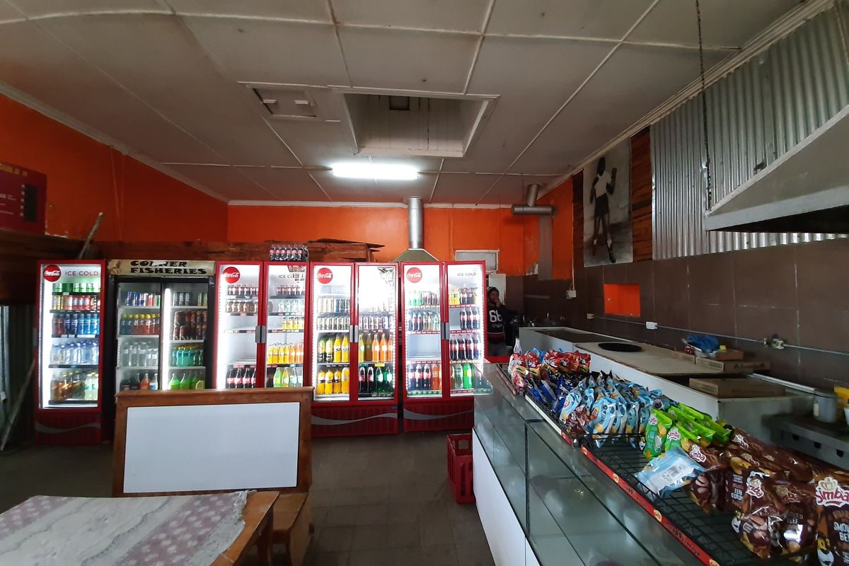 Commercial kitchen area featuring multiple glass-front display refrigerators, stainless steel prep counters, and tiled wall finishes in a functional retail setting.