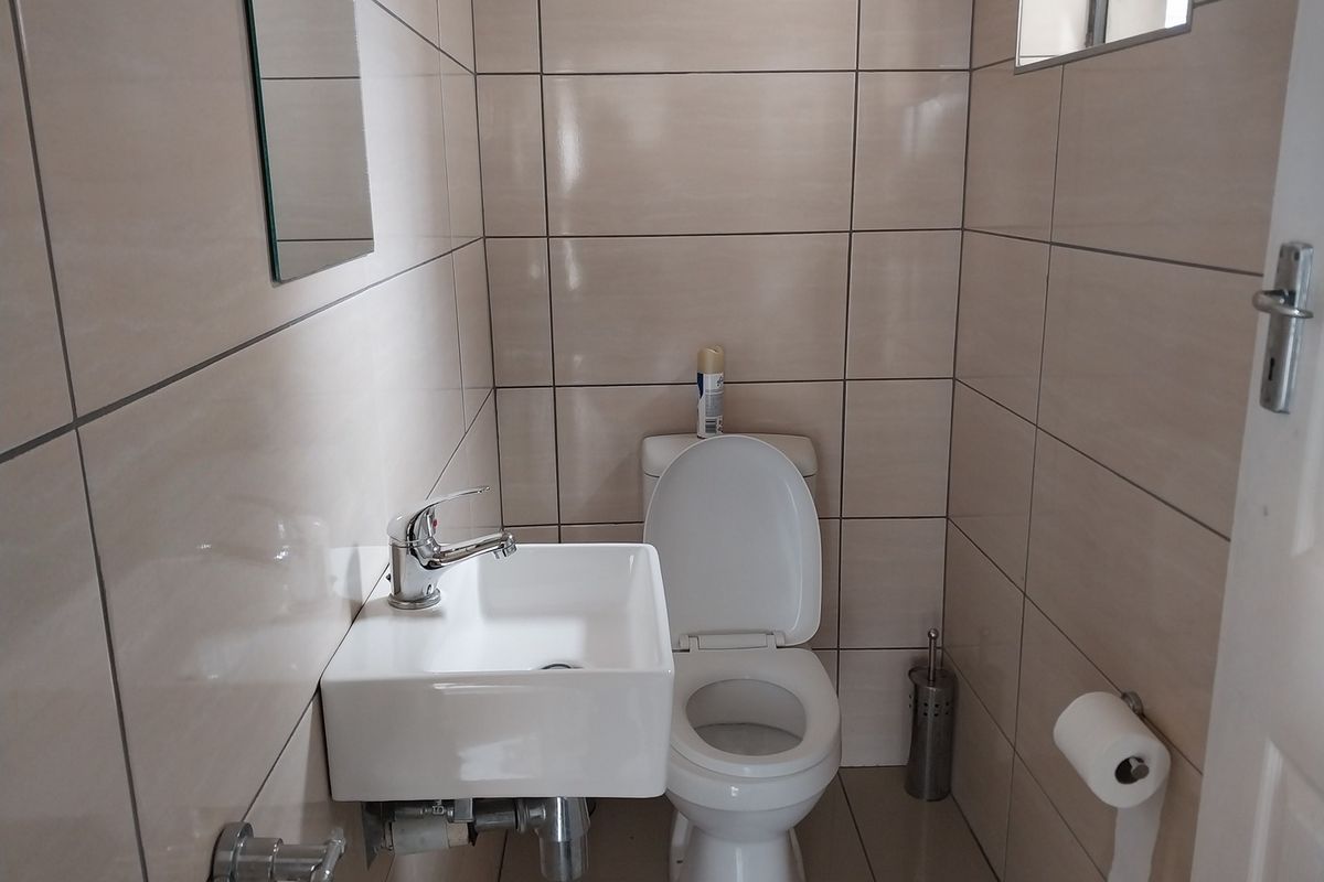 A compact guest bathroom featuring floor-to-ceiling ceramic tiling, a wall-mounted basin with chrome fixtures, and a standard toilet.