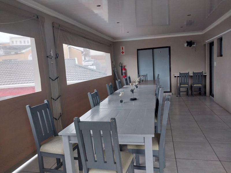 A covered patio area featuring tiled flooring, recessed ceiling lighting, and roll-up weather blinds, suitable for outdoor dining or guest house communal use.