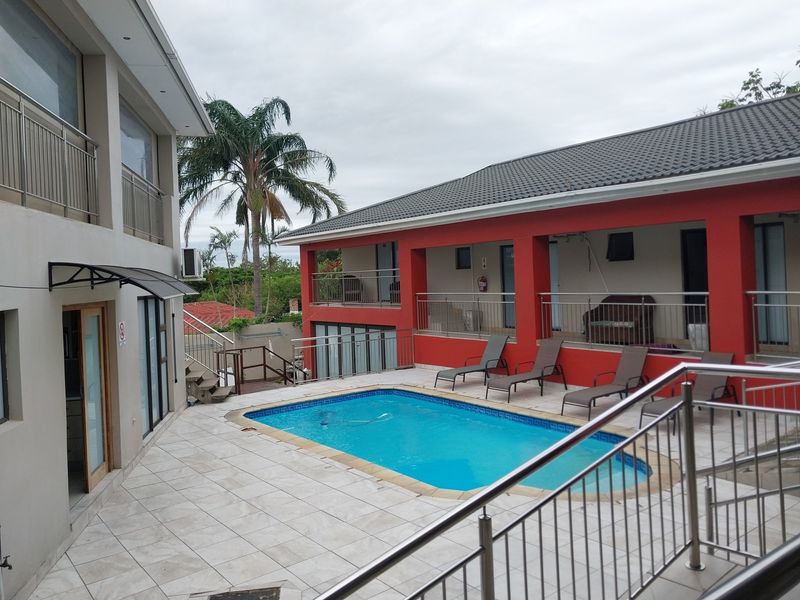 Outdoor pool area featuring a tiled deck, stainless steel balustrades, and covered patio access, set within a multi-level guest house property.
