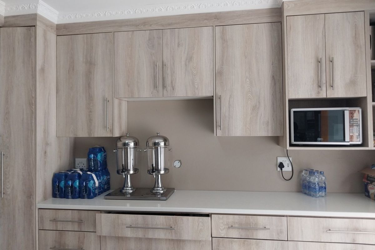 A well-maintained kitchen area featuring light wood-look cabinetry, white countertops, and a built-in microwave with decorative crown molding.